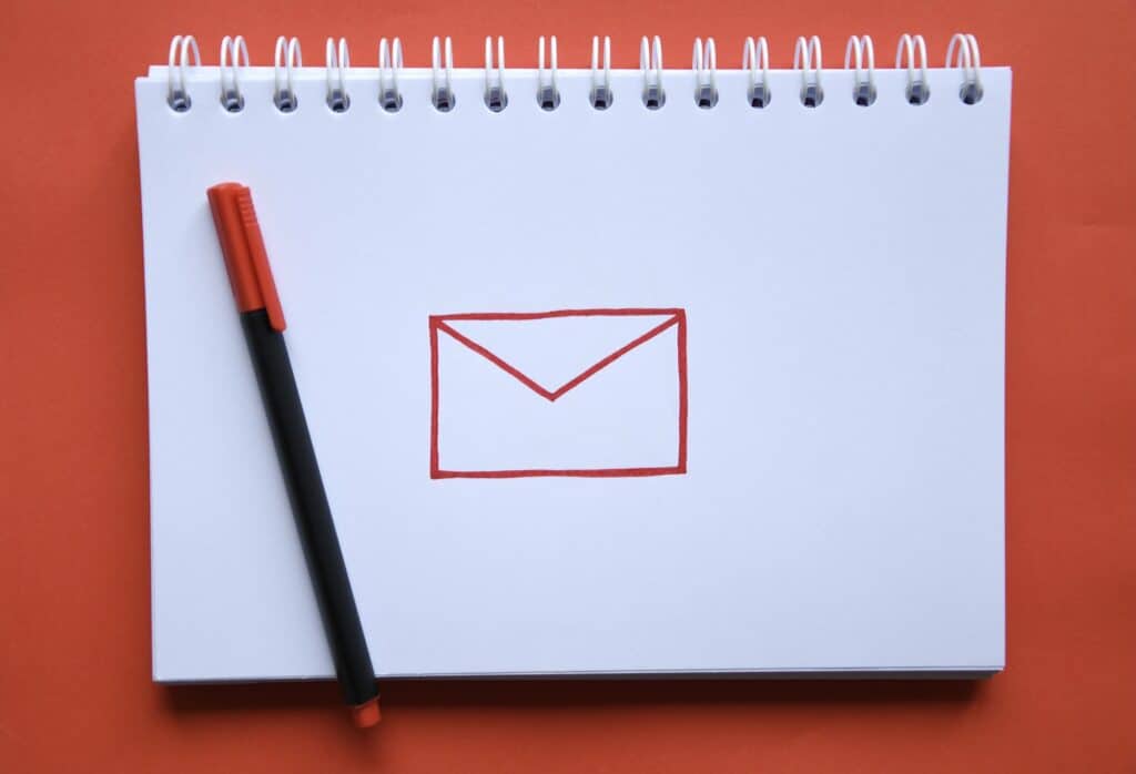 Overhead photo of a notebook with a drawing of a symbol for email and a pen on red background